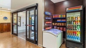 A hotel lobby with a glass door entrance, a refrigerated display case with beverages, and a wall-mounted shelf with snacks. - Best Western Plus Hobby Airport Inn & Suites (Houston)