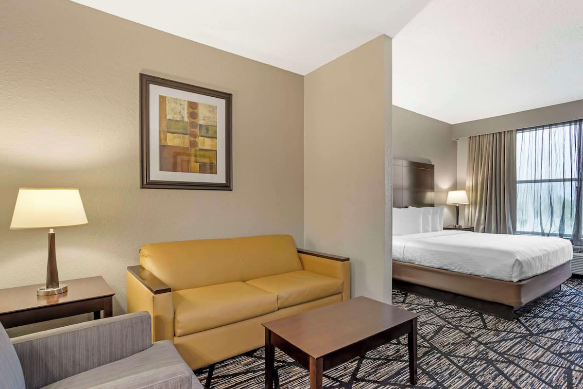 A hotel room with a bed, a sofa, a small table, a lamp, and a framed picture on the wall.