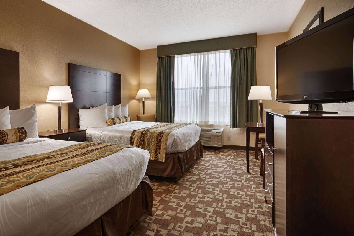 A hotel room with two beds, a television, and a window with curtains.