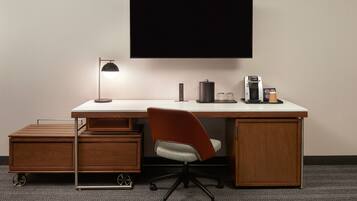 Ein moderner Schreibtisch mit Flachbildfernseher, einer Lampe, einer Kaffeemaschine und einem kleinen Schrank.