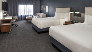 Une chambre d’hôtel avec deux lits, un bureau, une chaise, une télévision et une grande fenêtre avec des rideaux.