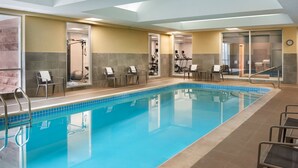 Une piscine intérieure à l’eau d’un bleu cristallin, entourée de chaises longues et d’appareils de musculation.