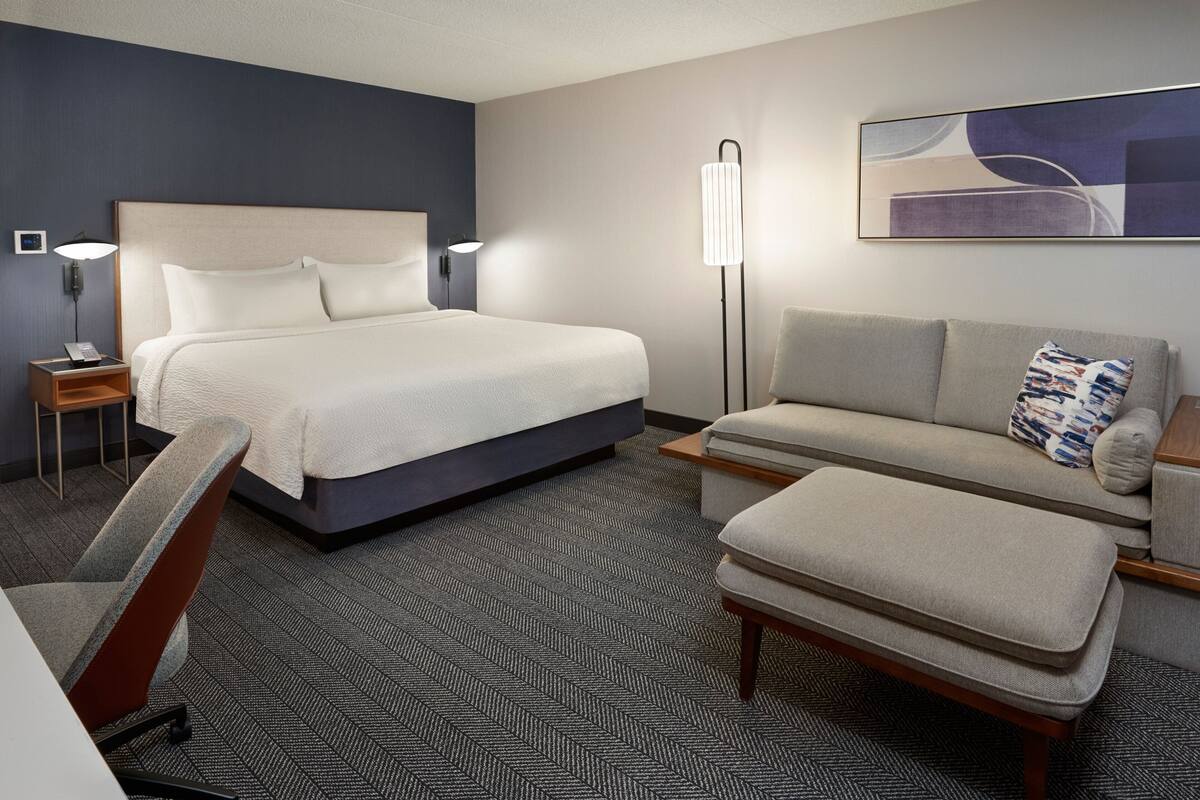 A hotel room with a bed, a sofa, a chair, a desk, and a lamp.