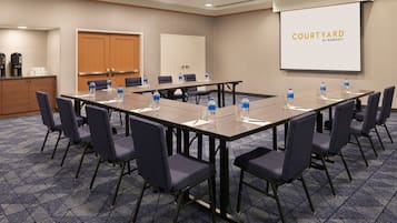 Un salón de conferencias con una larga mesa, sillas, botellas de agua y una pantalla de presentación que muestra "COURTYARD BY MARRIOTT".