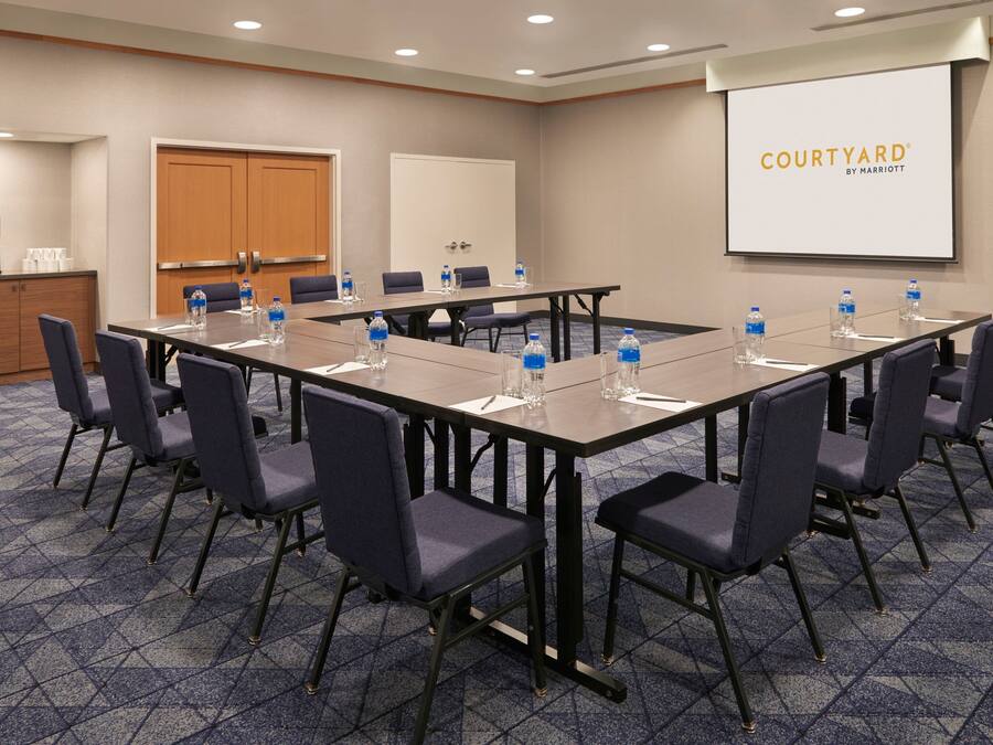 Un salón de conferencias con una larga mesa, sillas, botellas de agua y una pantalla de presentación que muestra "COURTYARD BY MARRIOTT".