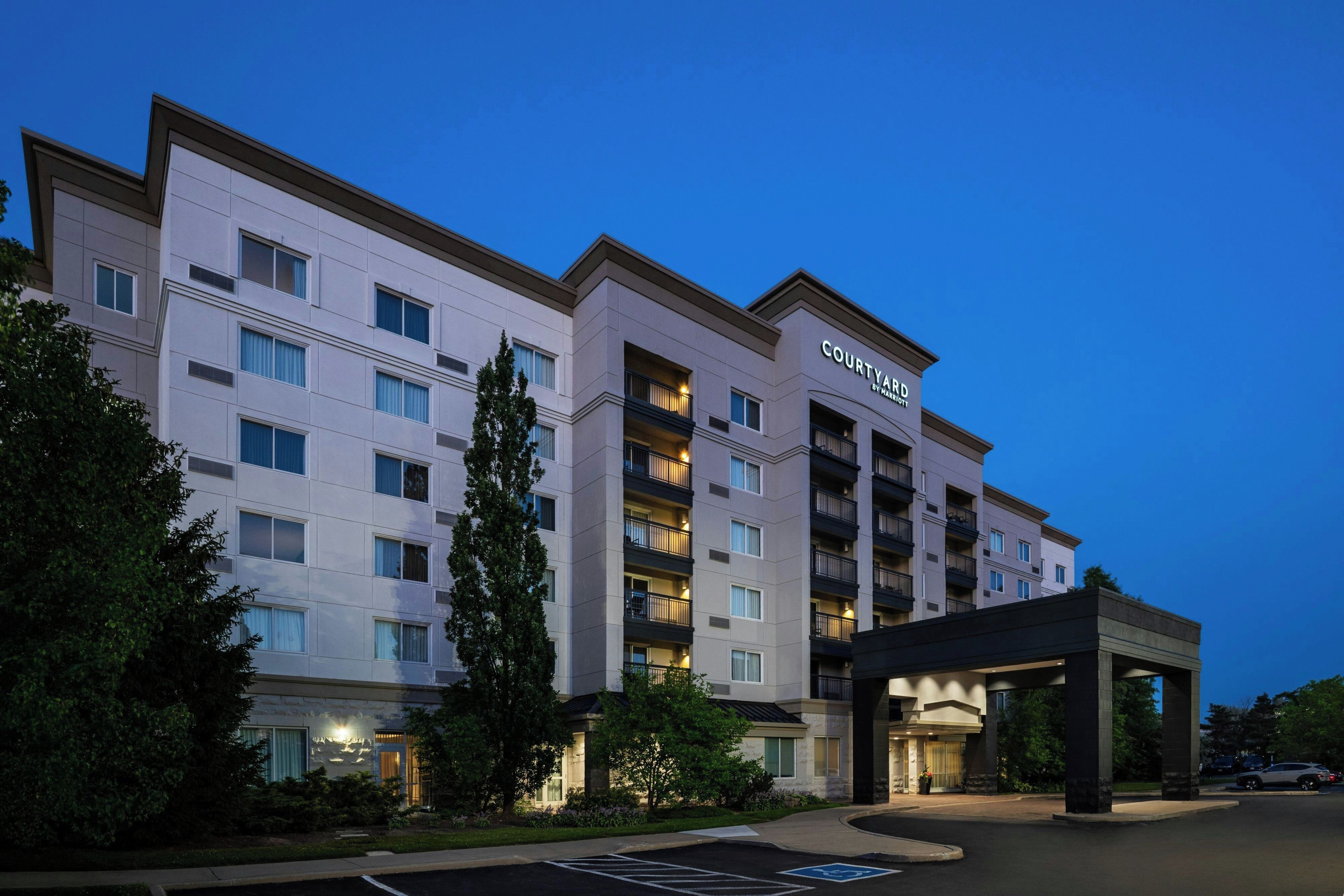 A multi-story hotel with a modern facade, a covered entrance, and a parking area with handicapped accessibility.
