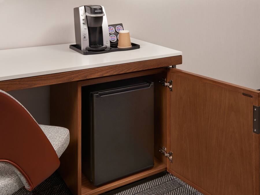 Una kitchenette compacta con cafetera, una pila de vasos de papel y un refrigerador pequeño.