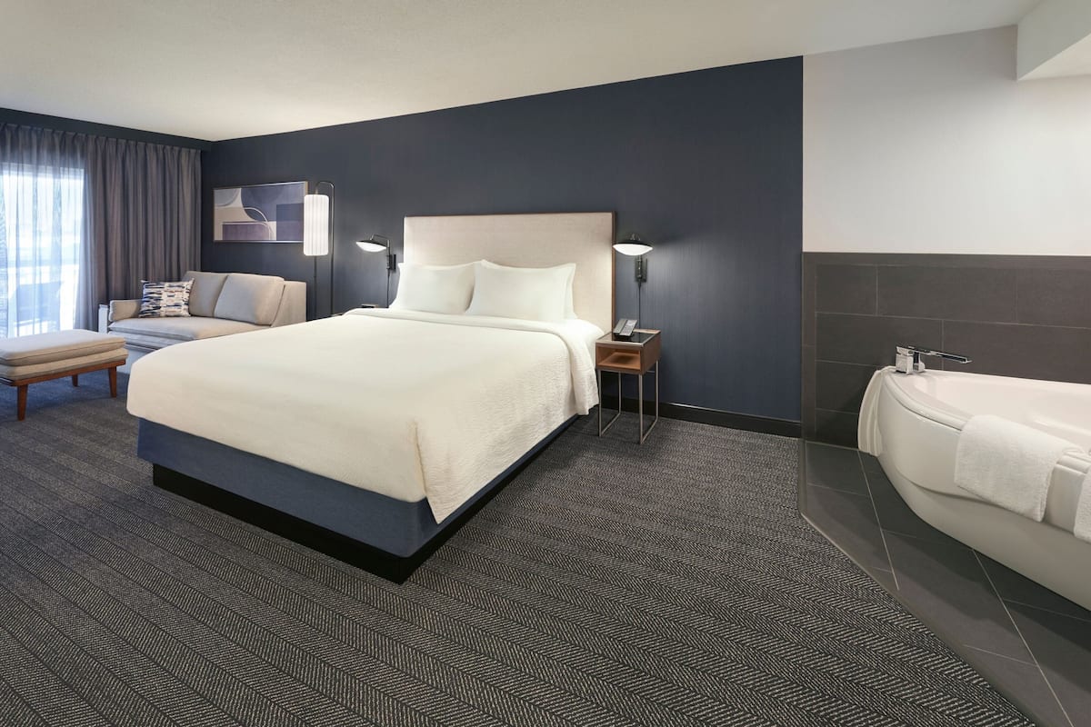 A hotel room with a large bed, a sofa, a desk, and a bathtub.