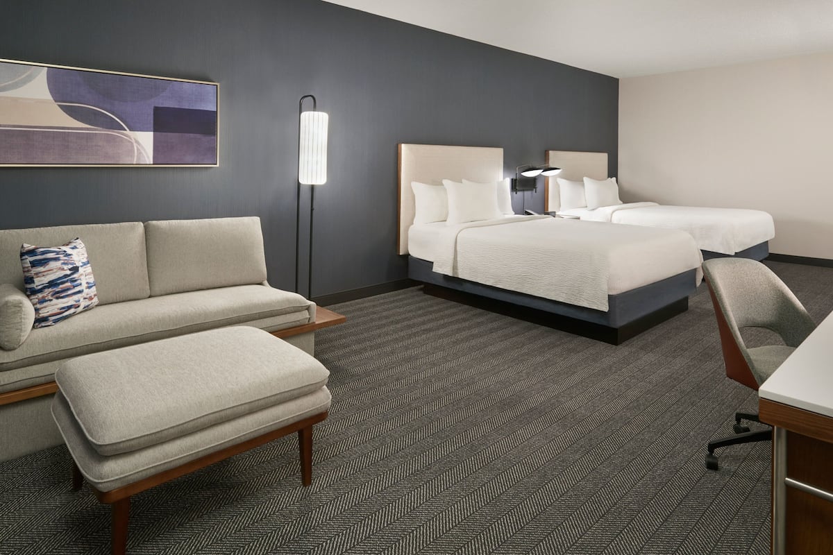 A hotel room with a large bed, a sofa, a desk, and a floor lamp.