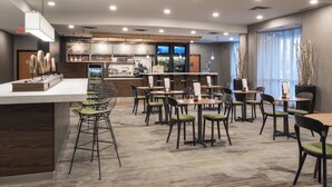 Un restaurante moderno con una zona de bar, varias opciones de asientos que incluyen sillas altas y mesas, y un tablero de menú visible.