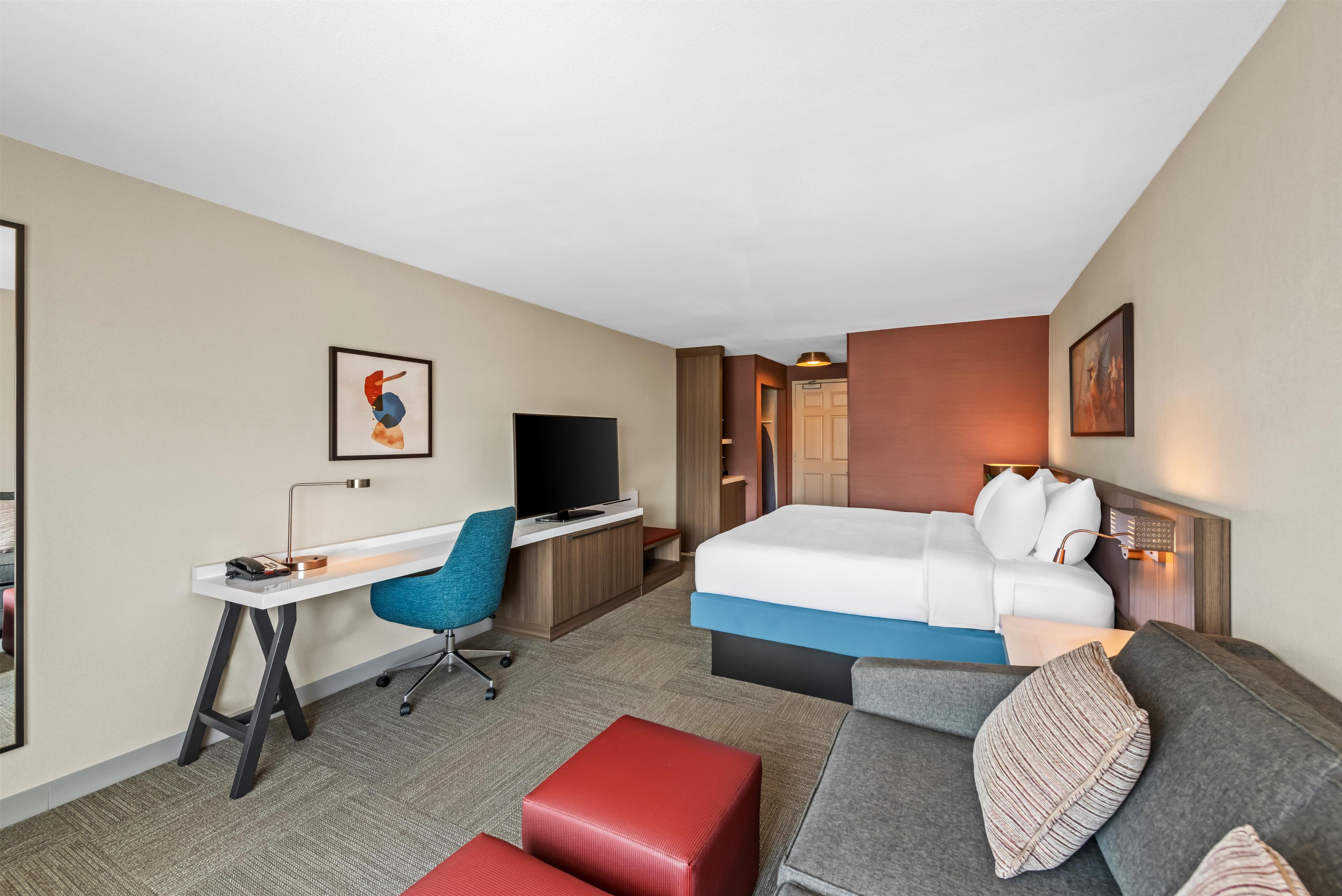 Quarto de hotel com cama, escrivaninha, cadeira, televisão e sofá.
