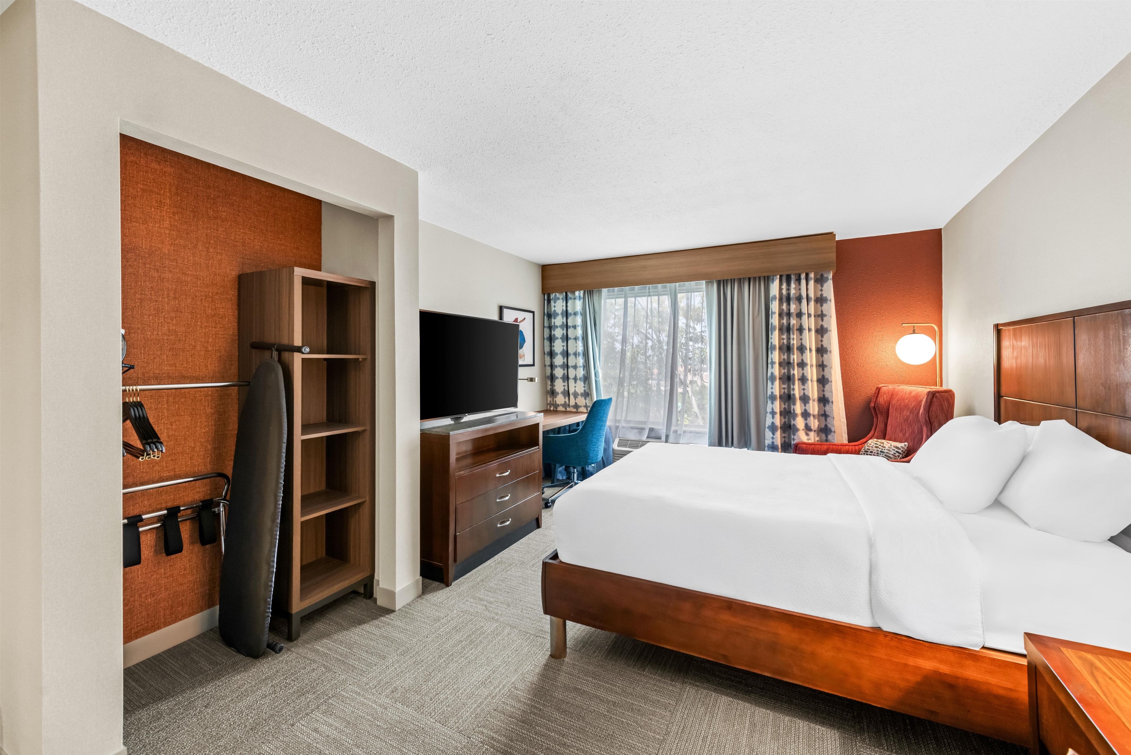 Ein Hotelzimmer mit Bett, Schreibtisch, Fernseher, Kleiderschrank und einem Fenster mit Vorhängen.