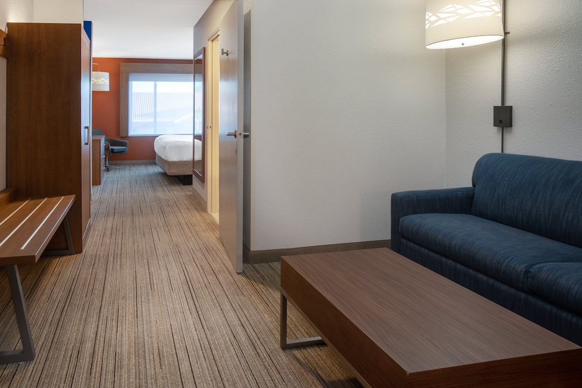 A hotel room with a wooden bench, a blue sofa, a lamp, and a bed in the background.