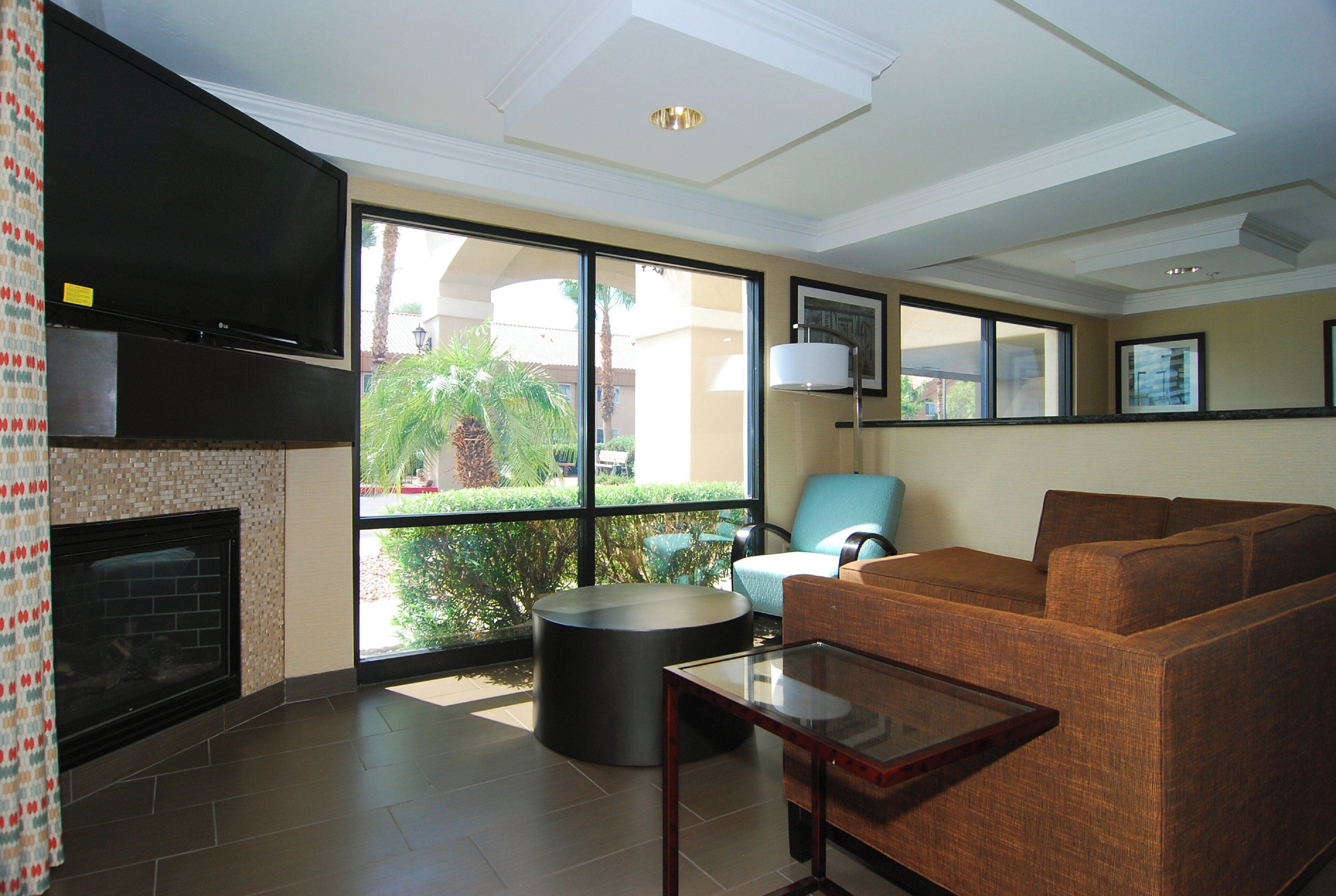 A modern living room with a fireplace, comfortable seating, and large windows offering a view of greenery.