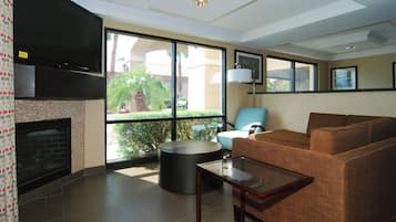 A modern living room with a fireplace, comfortable seating, and large windows offering a view of greenery.