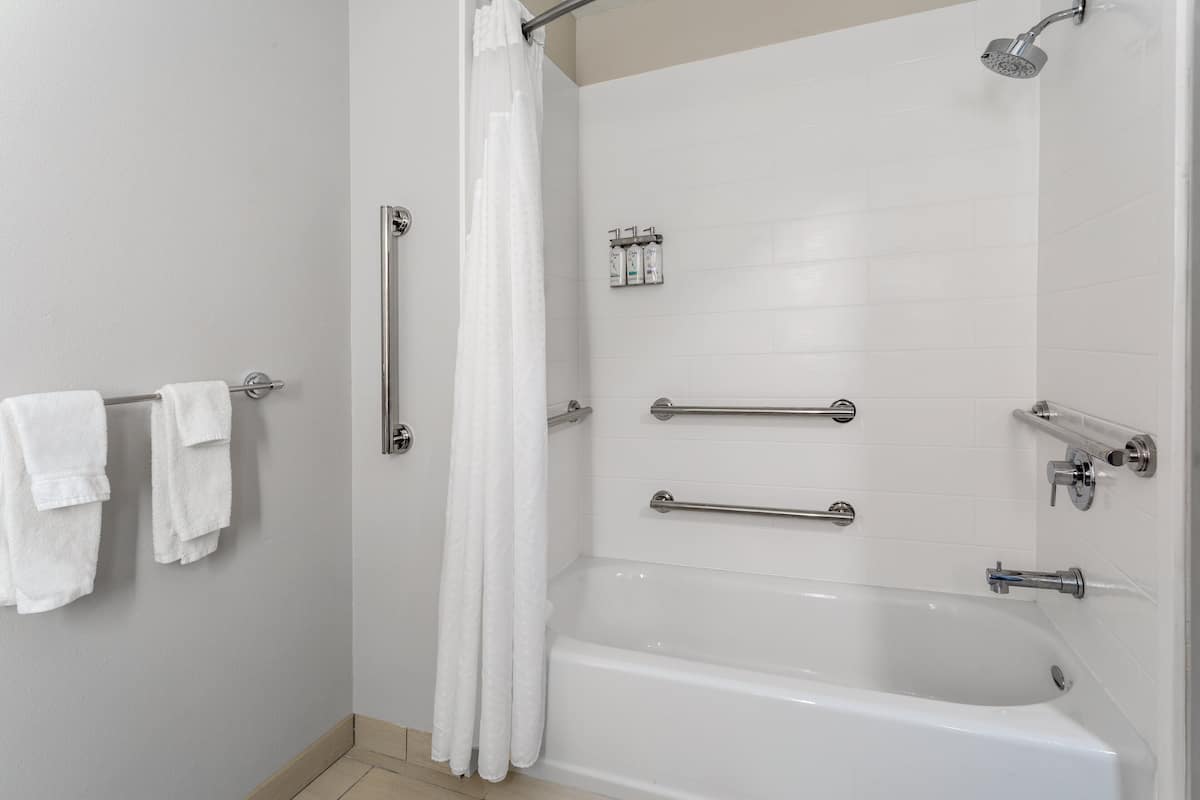 A modern bathroom with a bathtub, shower, and handrails.