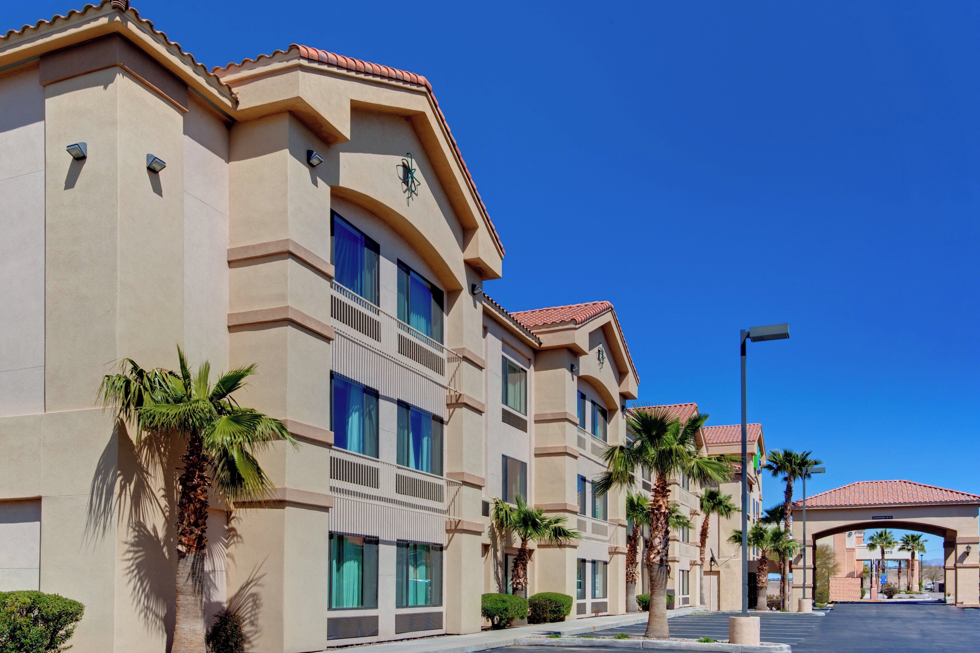 A multi-story hotel with a flat roof, large windows, and palm trees in the foreground.