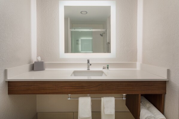 A bathroom with a white sink, wooden vanity, and a mirror.