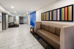 Een moderne lobby met een visgraatvloer, een bruine leren bank en een kleurrijk abstract kunstwerk aan de muur.