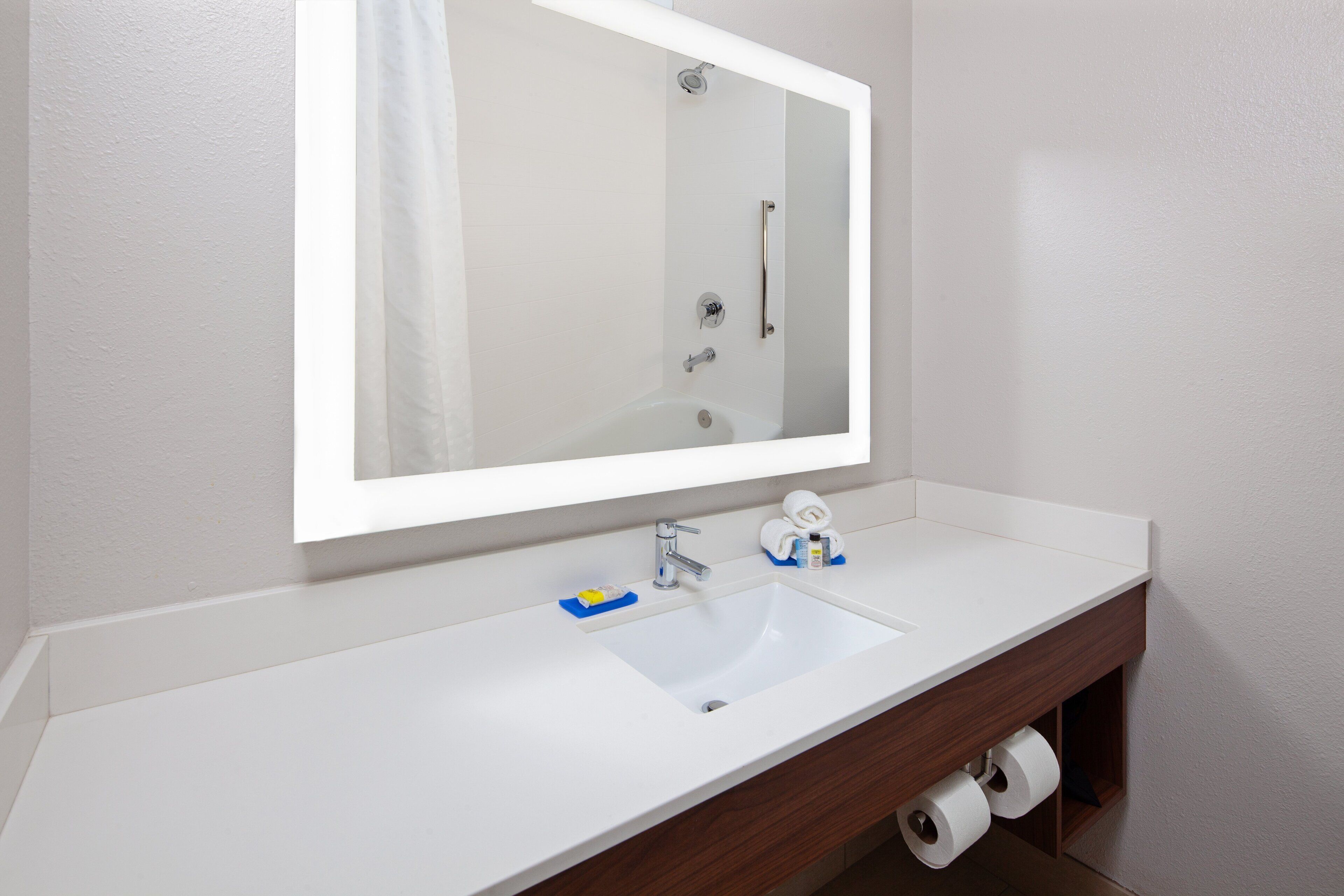 A bathroom with a white sink, a large mirror, and a wooden vanity.