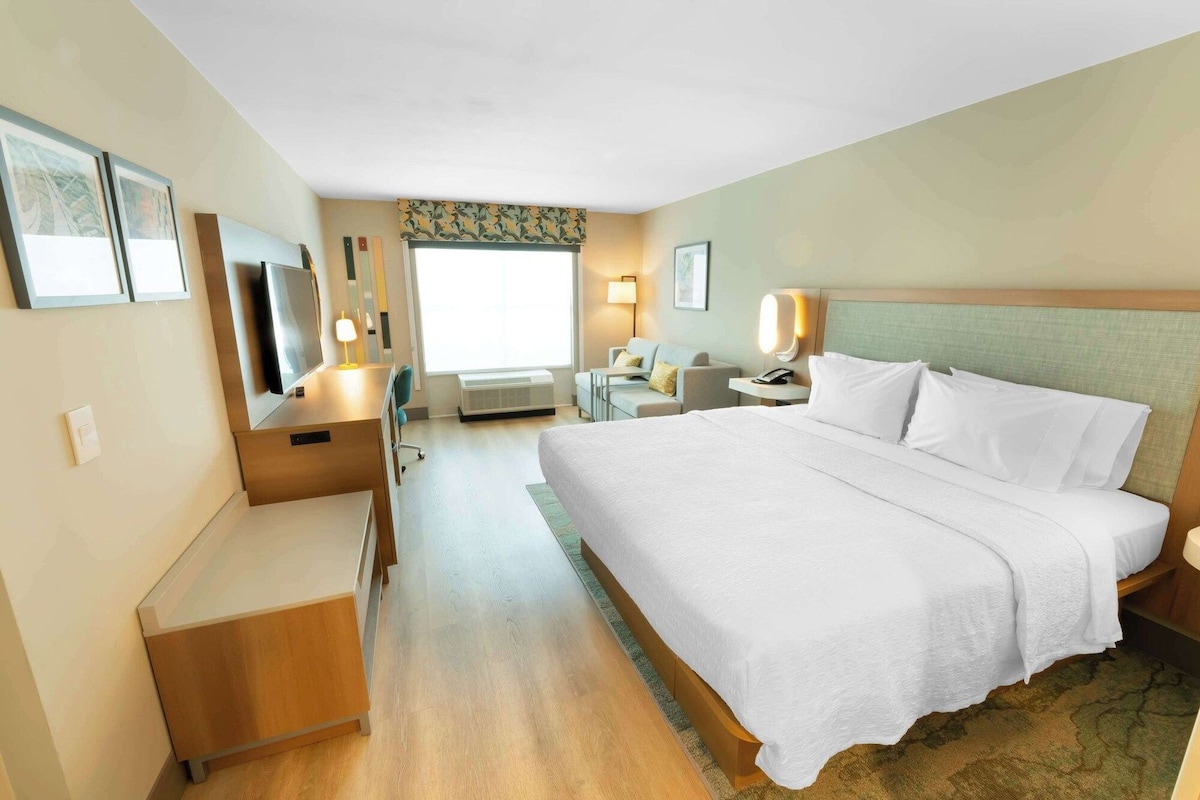 A hotel room with a bed, desk, chair, and a small seating area.