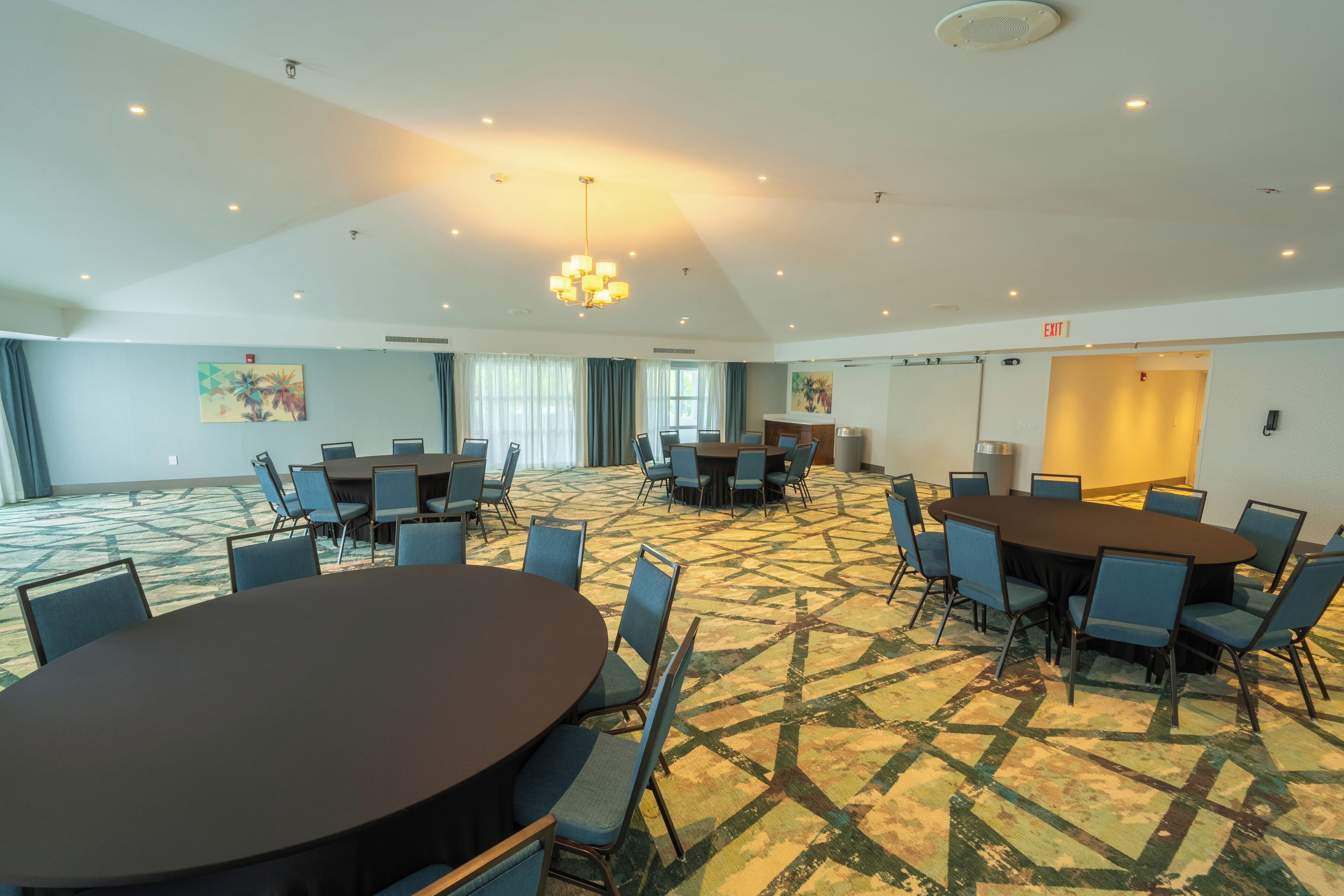 A conference room with multiple tables and chairs, a patterned carpet, and ceiling lights.
