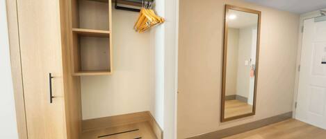 A room with a wooden wardrobe, a mirror, and a wooden floor.
