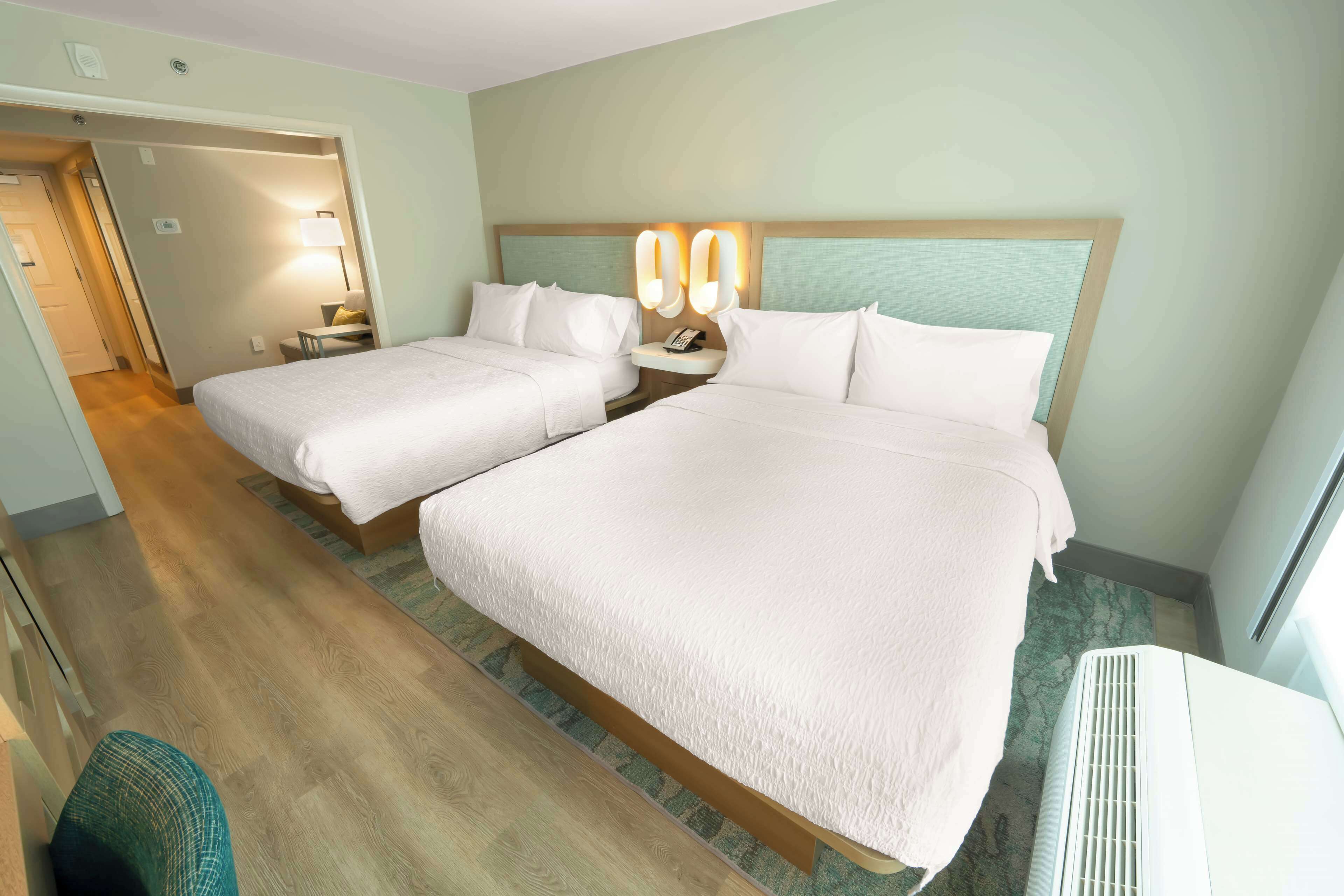 Ein Hotelzimmer mit zwei Betten, einem Nachttisch mit Lampe, einem Telefon und einem fest installierten Heizkörper.