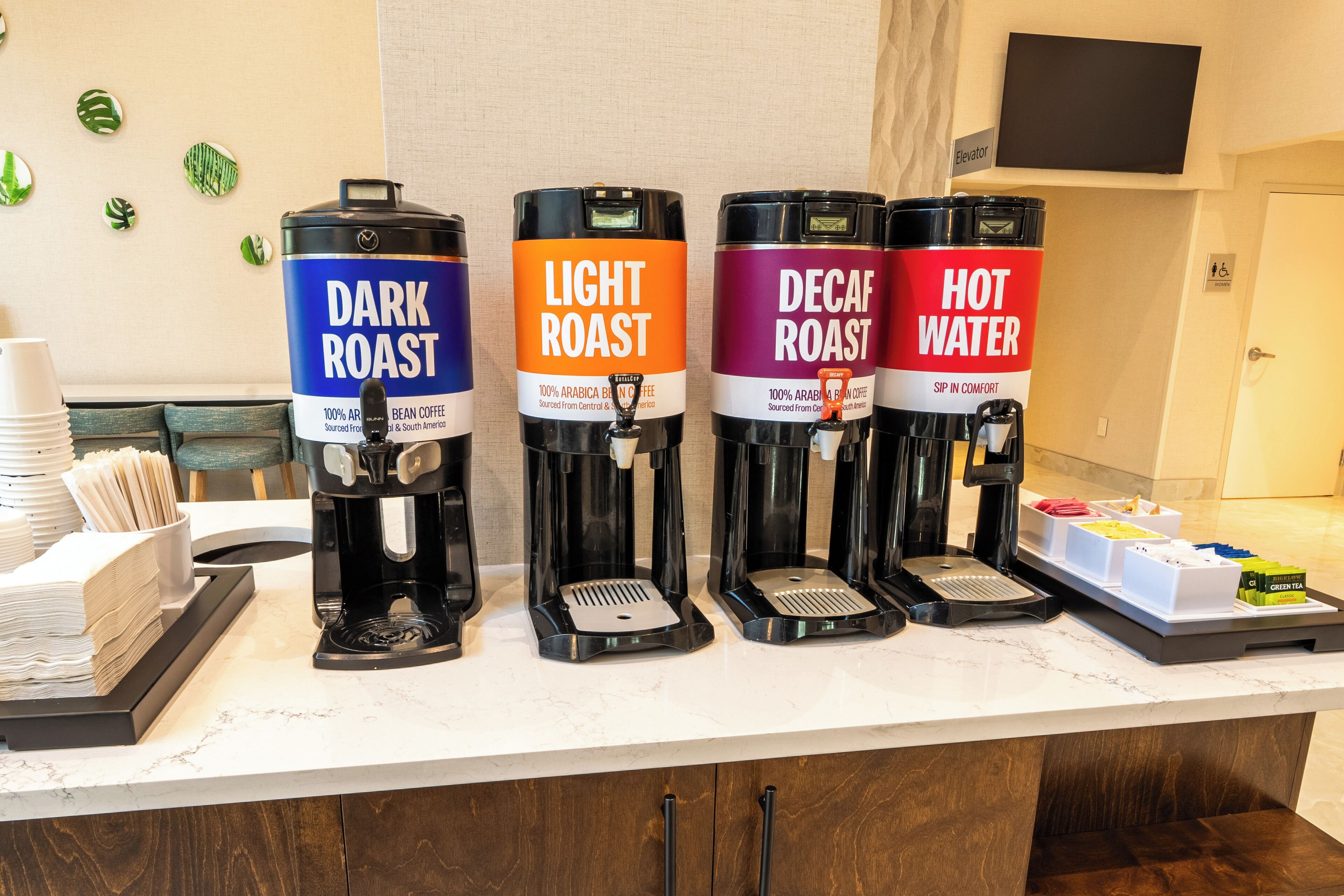 Una estación de café con cuatro dispensadores etiquetados como 'Dark Roast', 'Light Roast', 'Decaf Roast' y 'Agua Caliente'.