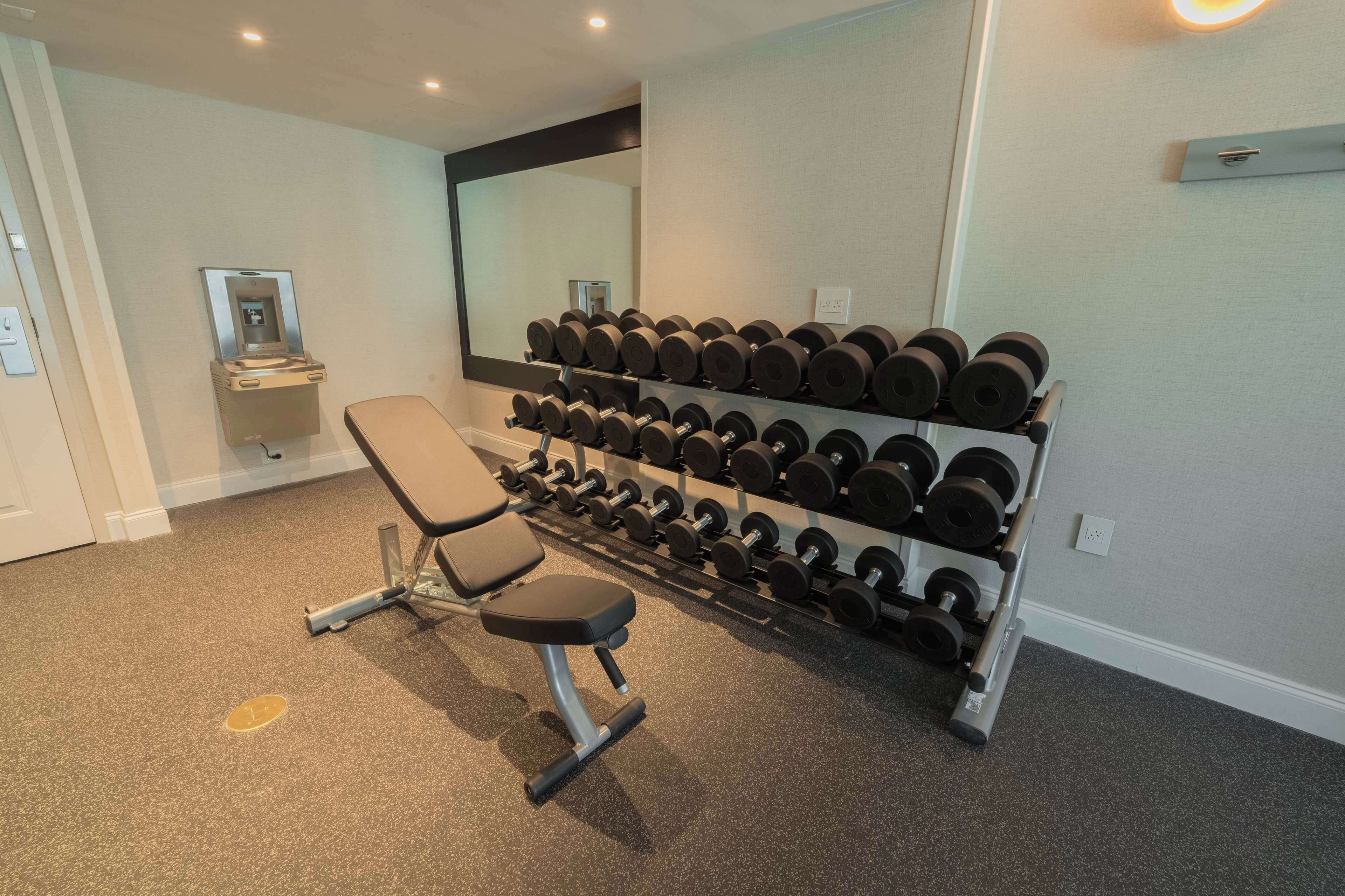 A gym with a bench, a rack of dumbbells, and a water dispenser.
