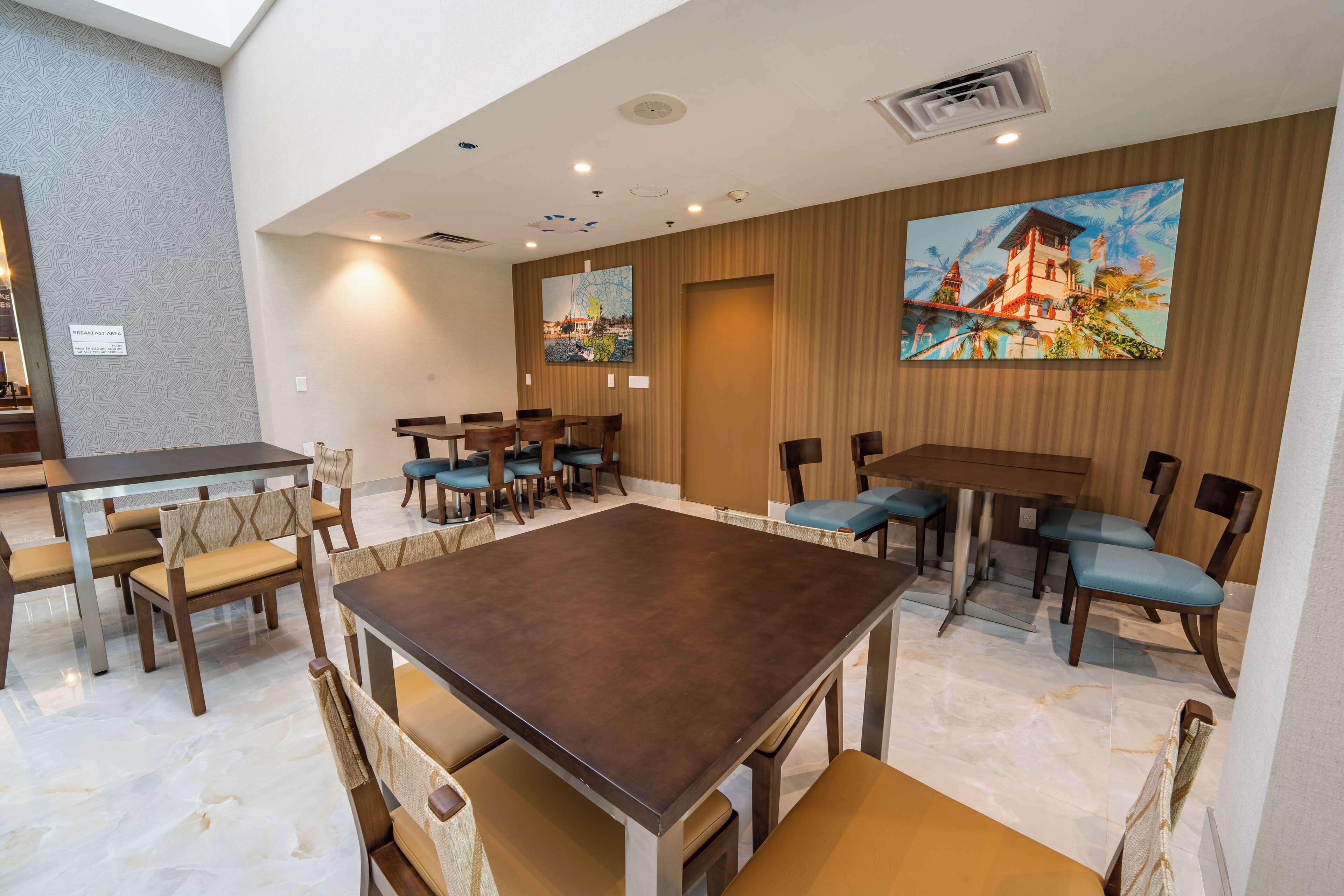 A hotel dining area with multiple tables and chairs, a large painting on the wall, and a sign indicating the breakfast area.