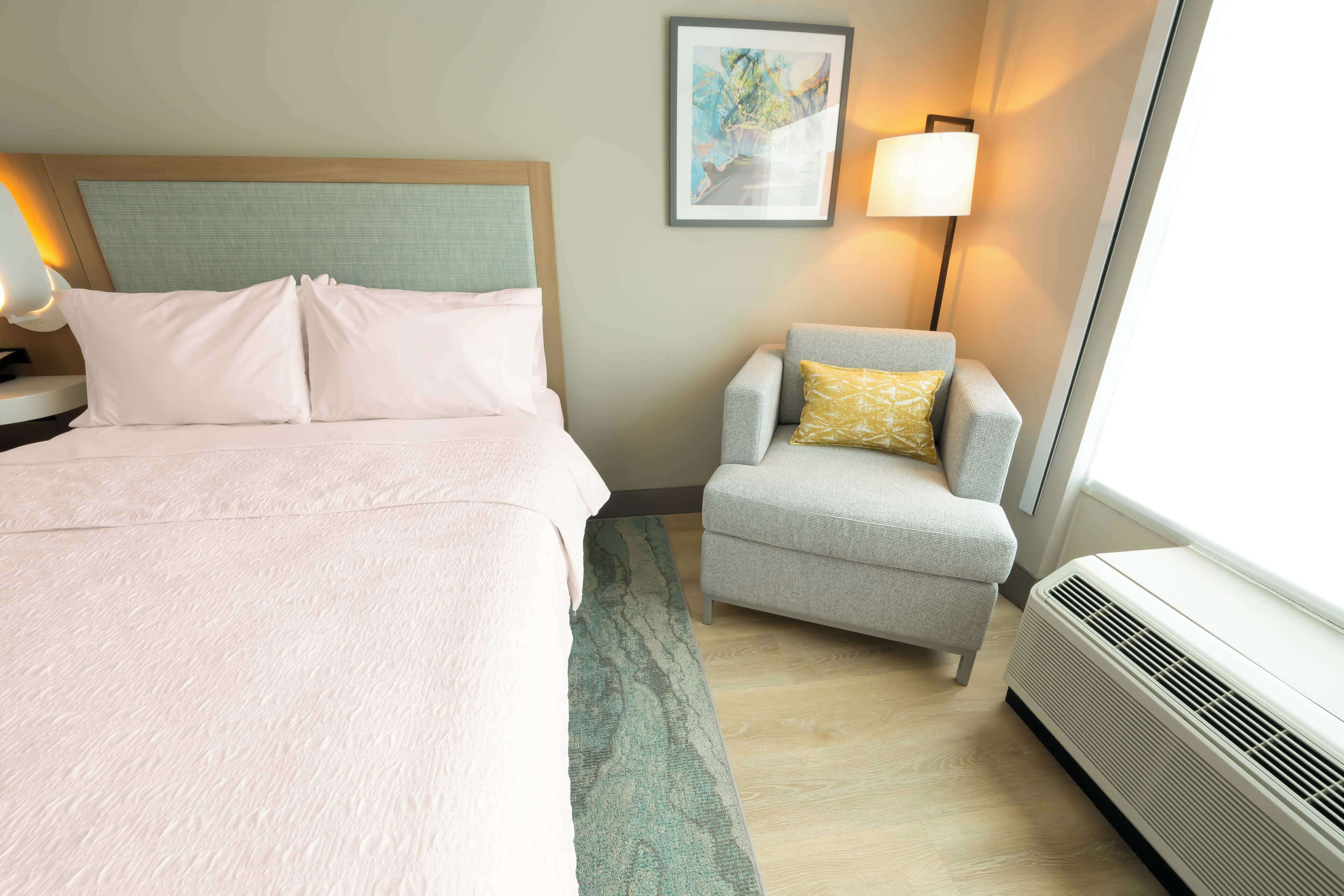 Quarto de hotel com cama, cadeira, abajur e aquecedor.