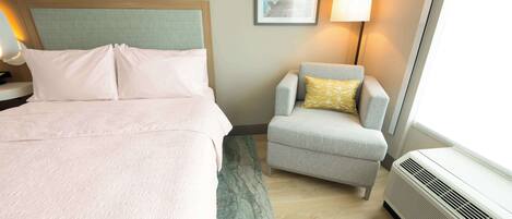 Quarto de hotel com cama, cadeira, abajur e aquecedor.
