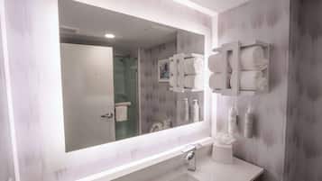 Une salle de bain moderne avec un grand miroir, un meuble-lavabo blanc et un espace douche.