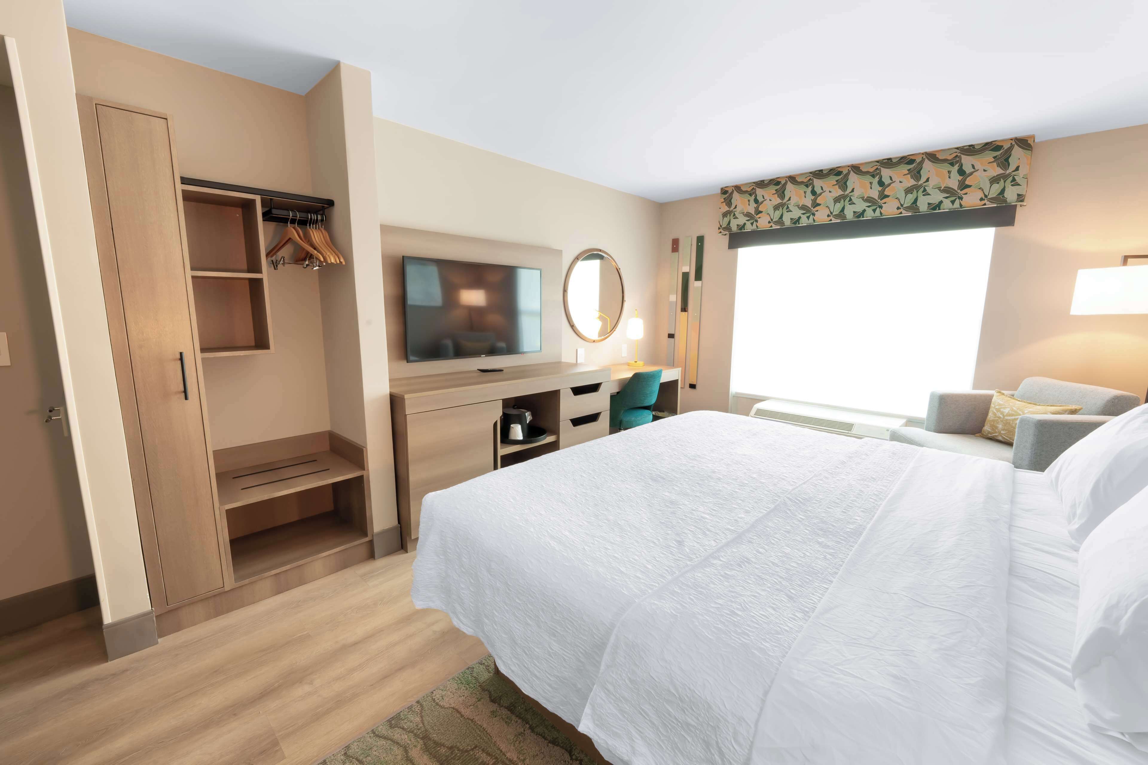 Une chambre d’hôtel avec un grand lit, une télévision, un bureau avec une chaise, une armoire et une fenêtre donnant sur un beau paysage.