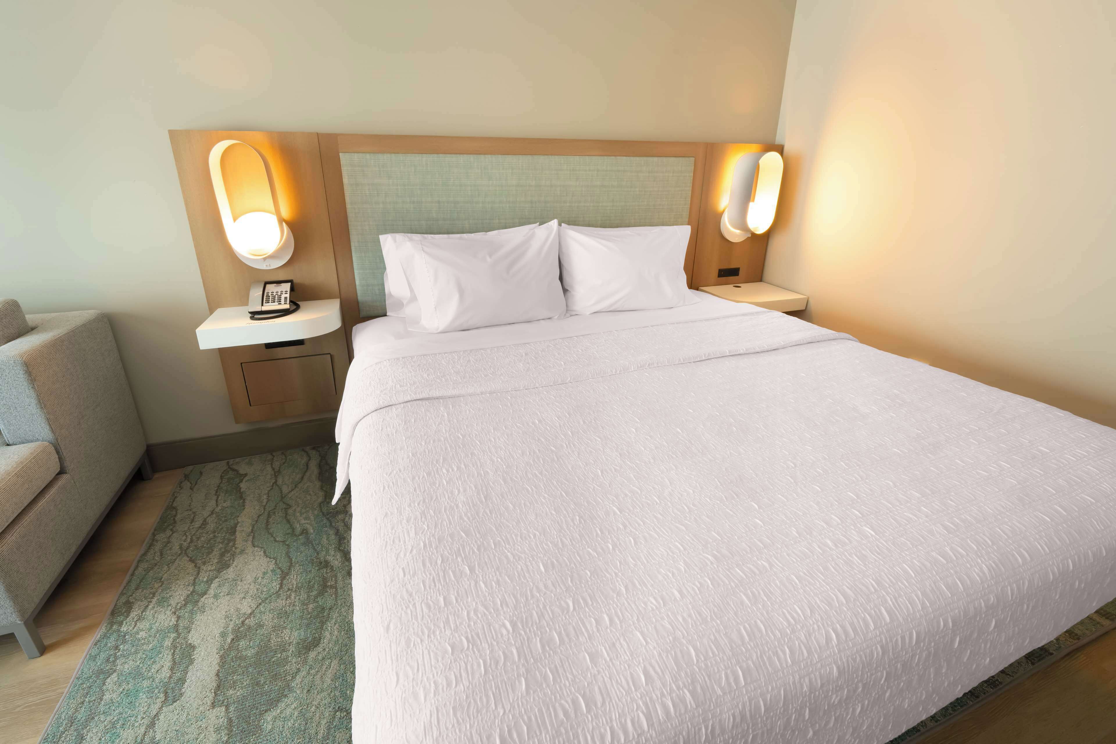 Una habitación de hotel con una cama grande, dos mesitas de noche con lámparas, un pequeño sofá y una alfombra estampada.