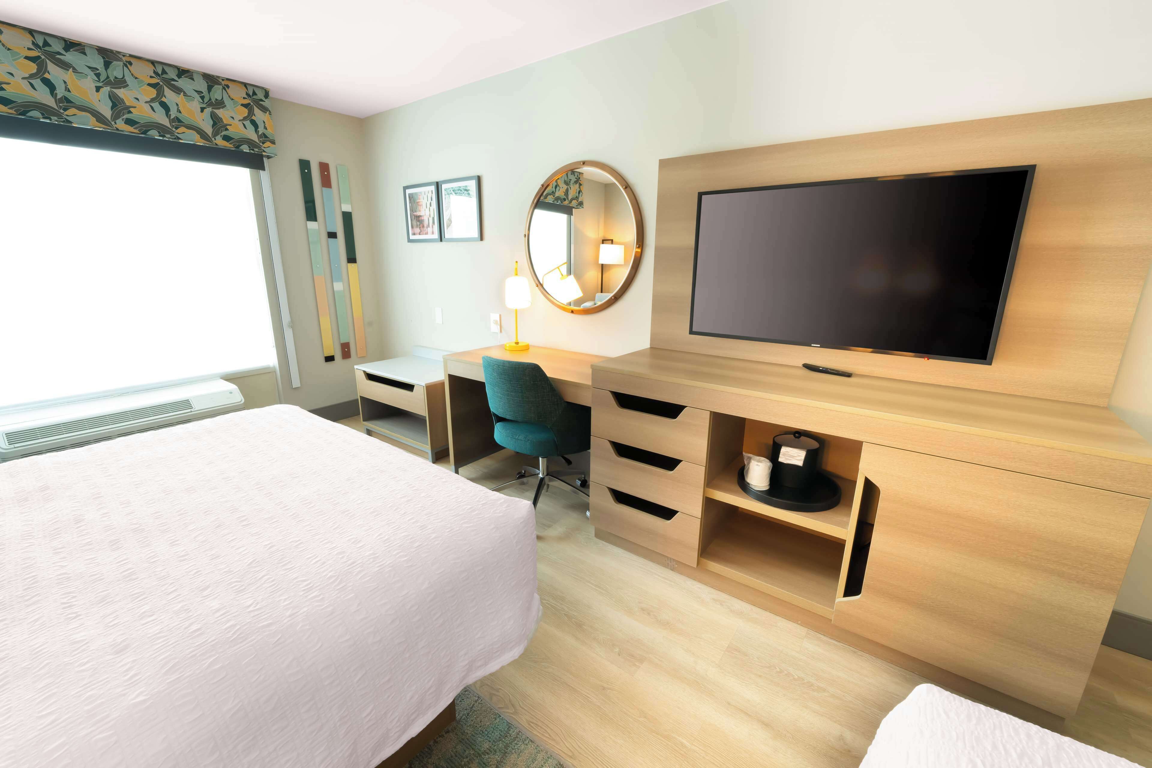Une chambre d’hôtel avec un lit, un bureau, une chaise, une télévision et une fenêtre.