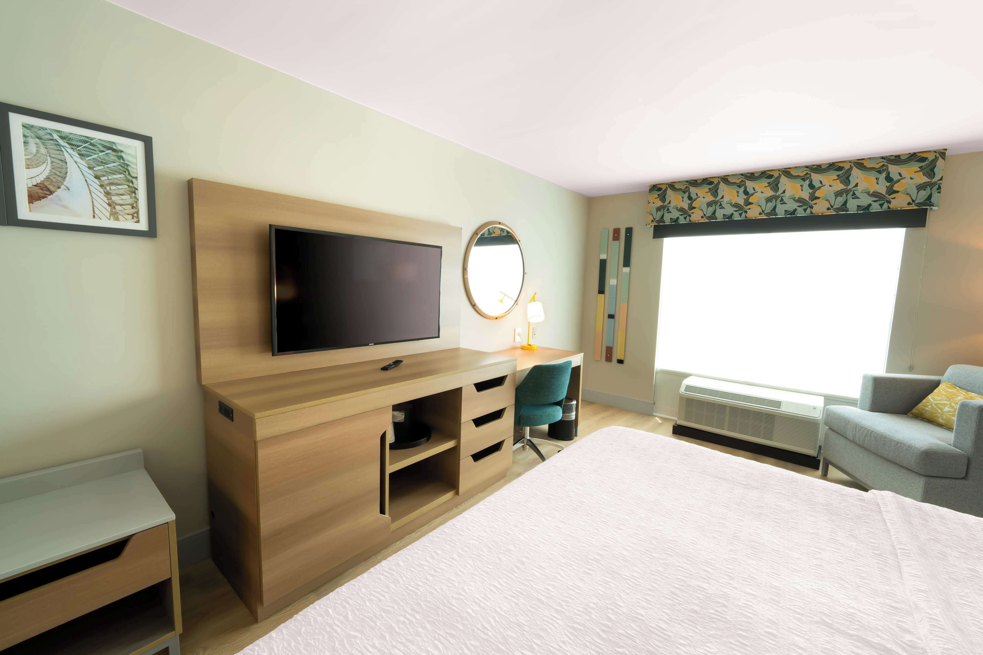 Hotellihuone, jossa on sänky, televisio, vetolaatikkoilla varustettu työpöytä, tuoli, ikkuna, josta on näkymä, ja seinälle kiinnitetty peili.