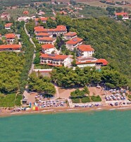 Vista aérea de un complejo turístico costero con varias edificaciones, una playa y un puerto deportivo.