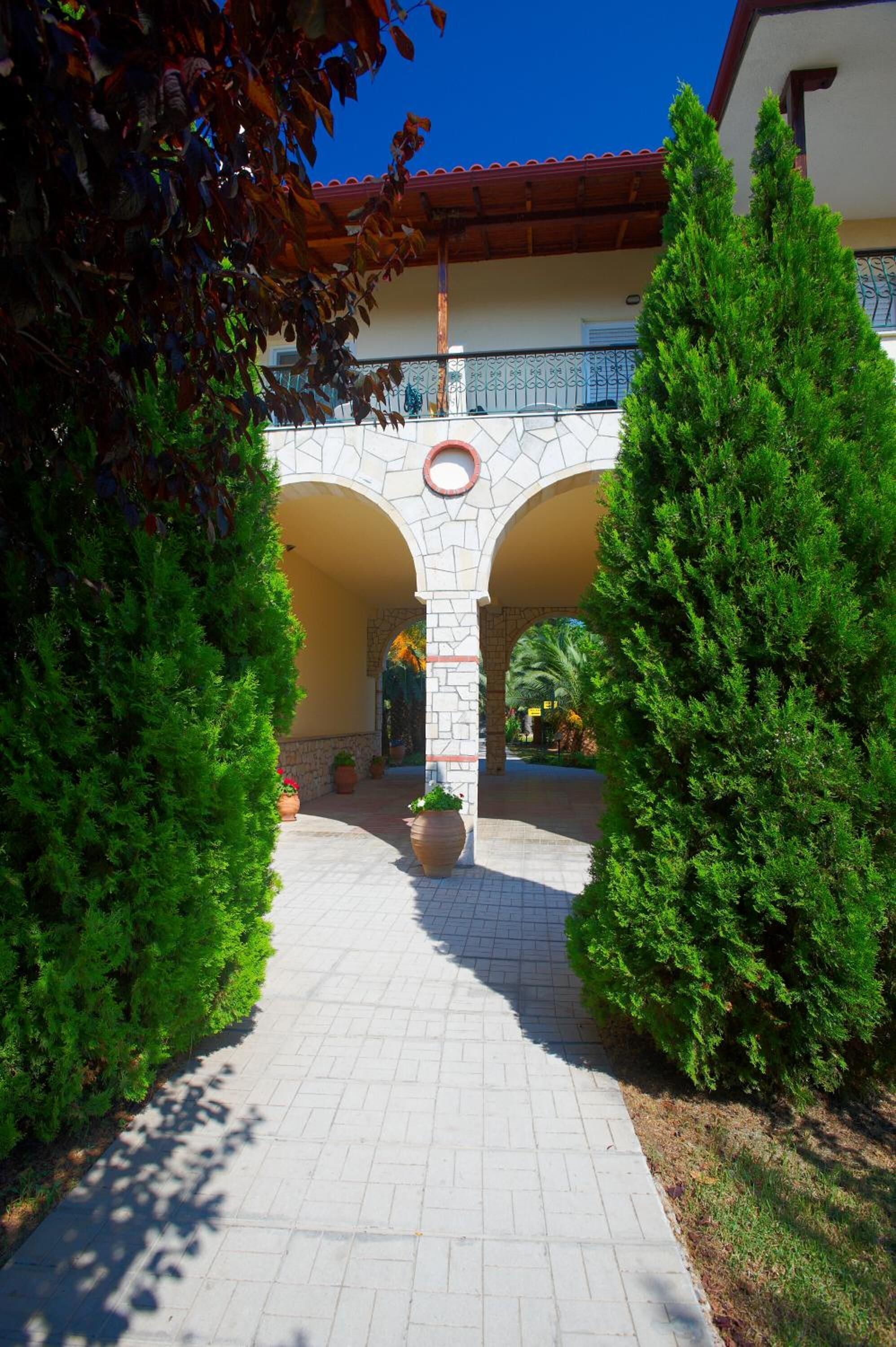 A paved pathway leading to a building with a stone archway, surrounded by green shrubs.