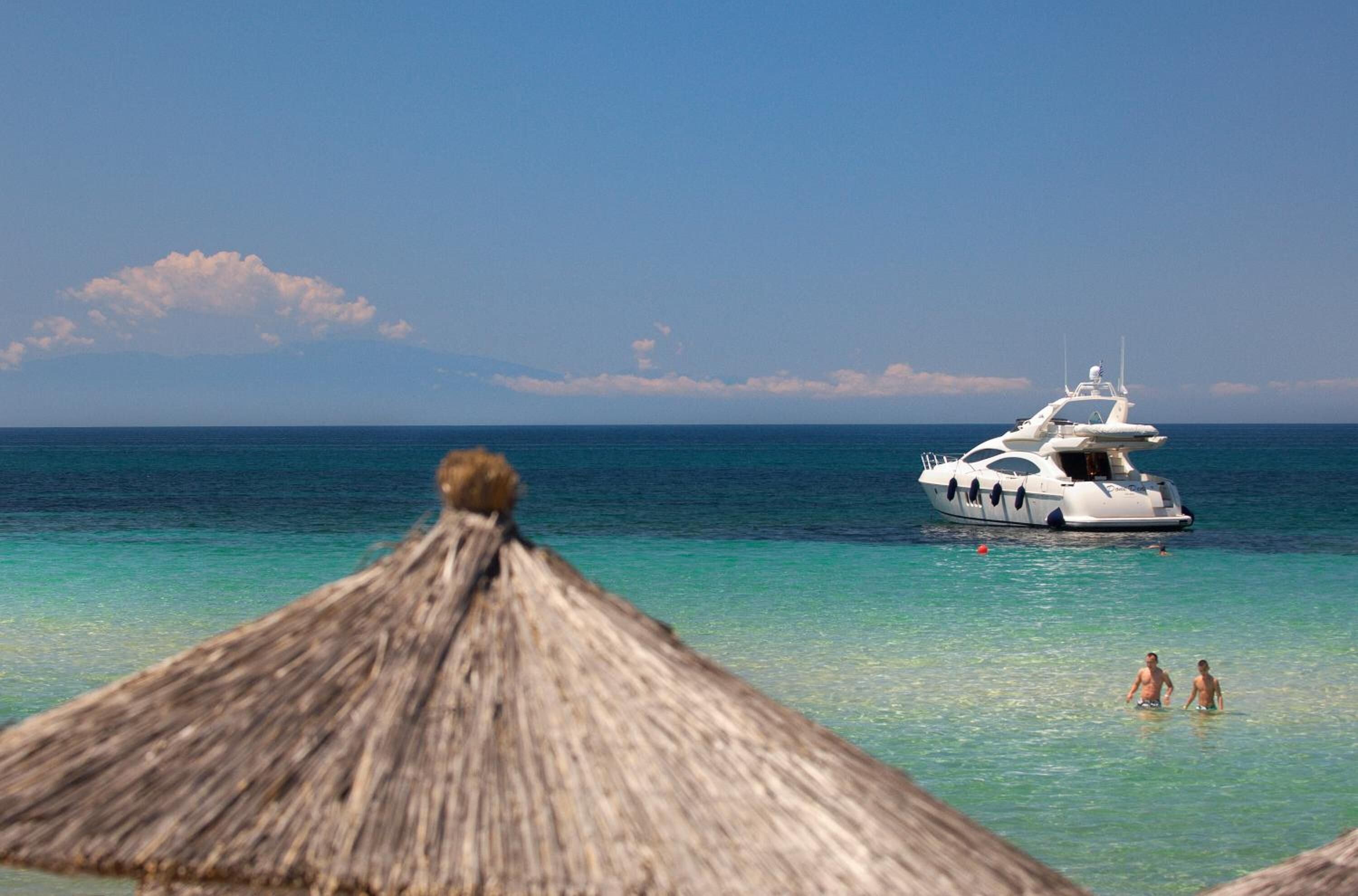 Une scène de plage avec un yacht blanc sur l’eau et deux personnes qui nagent.
