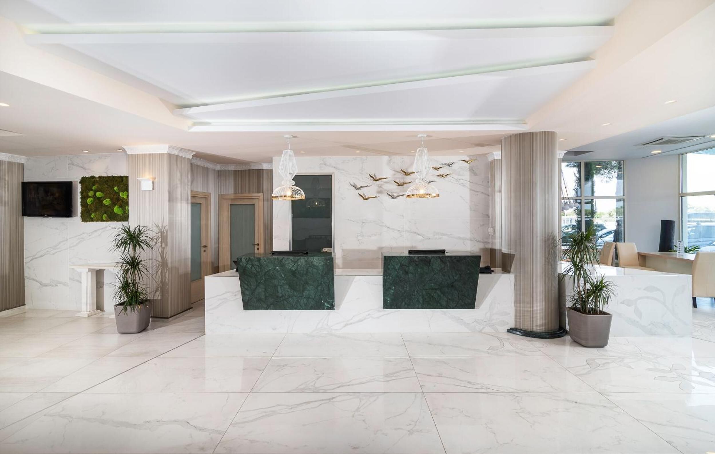 Un hall d’hôtel moderne avec un sol en marbre, un comptoir d’accueil et deux espaces aménagés pour s’asseoir.