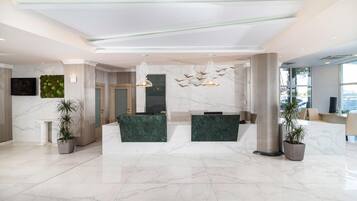 Un hall d’hôtel moderne avec un sol en marbre, un comptoir d’accueil et deux espaces aménagés pour s’asseoir.