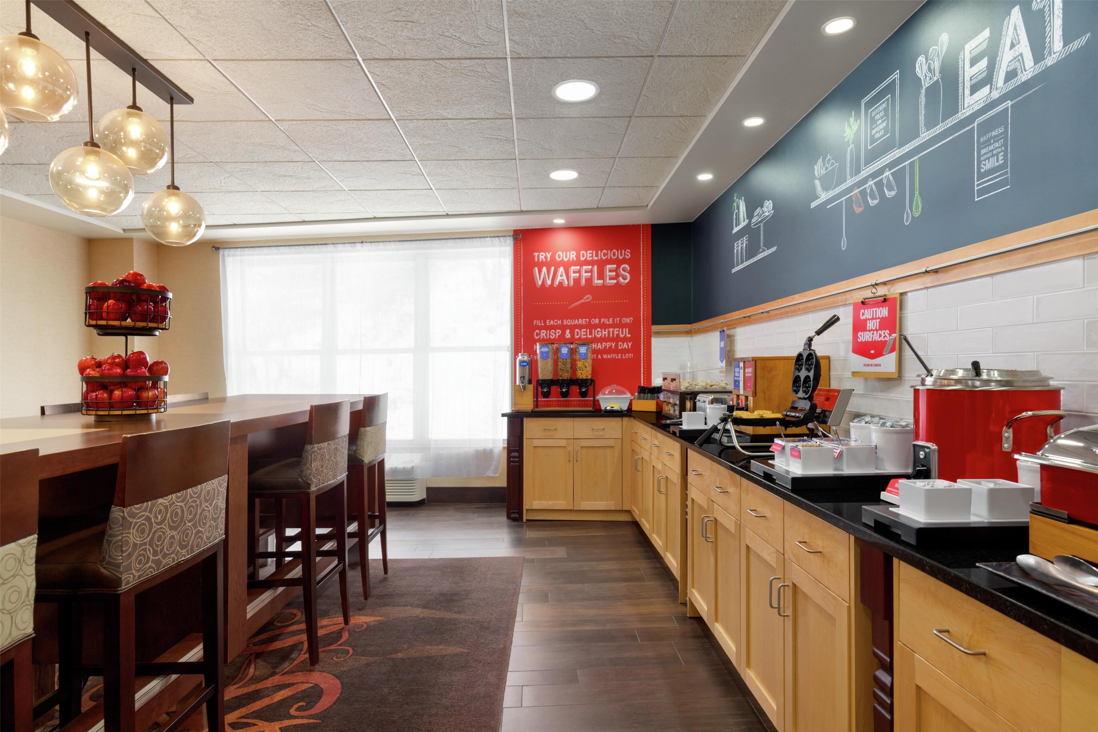 Una cocina de hotel con armarios de madera, encimera negra y estación de waffles.