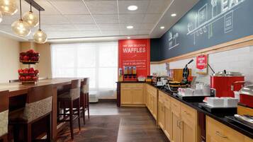 Una cocina de hotel con armarios de madera, encimera negra y estación de waffles.