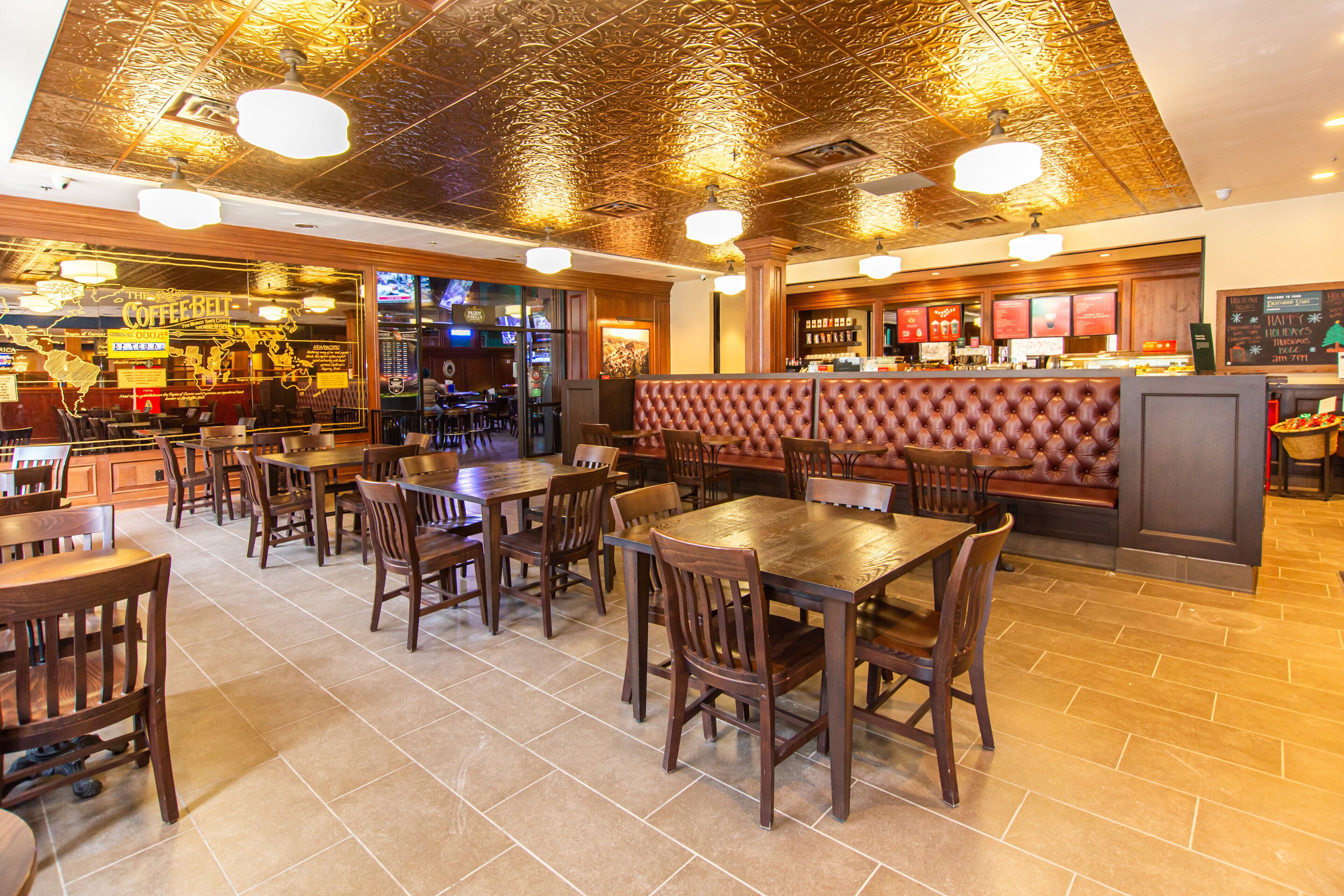 A restaurant interior with wooden tables and chairs, a bar area, and a cushioned booth seating.