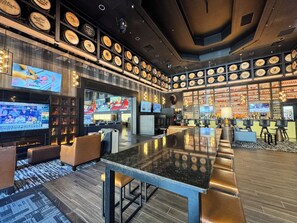 A bar area with a long counter, multiple seating options, and a wall decorated with circular plaques. - Hampton Inn Deadwood at Tin Lizzie Gaming Resort (Deadwood)