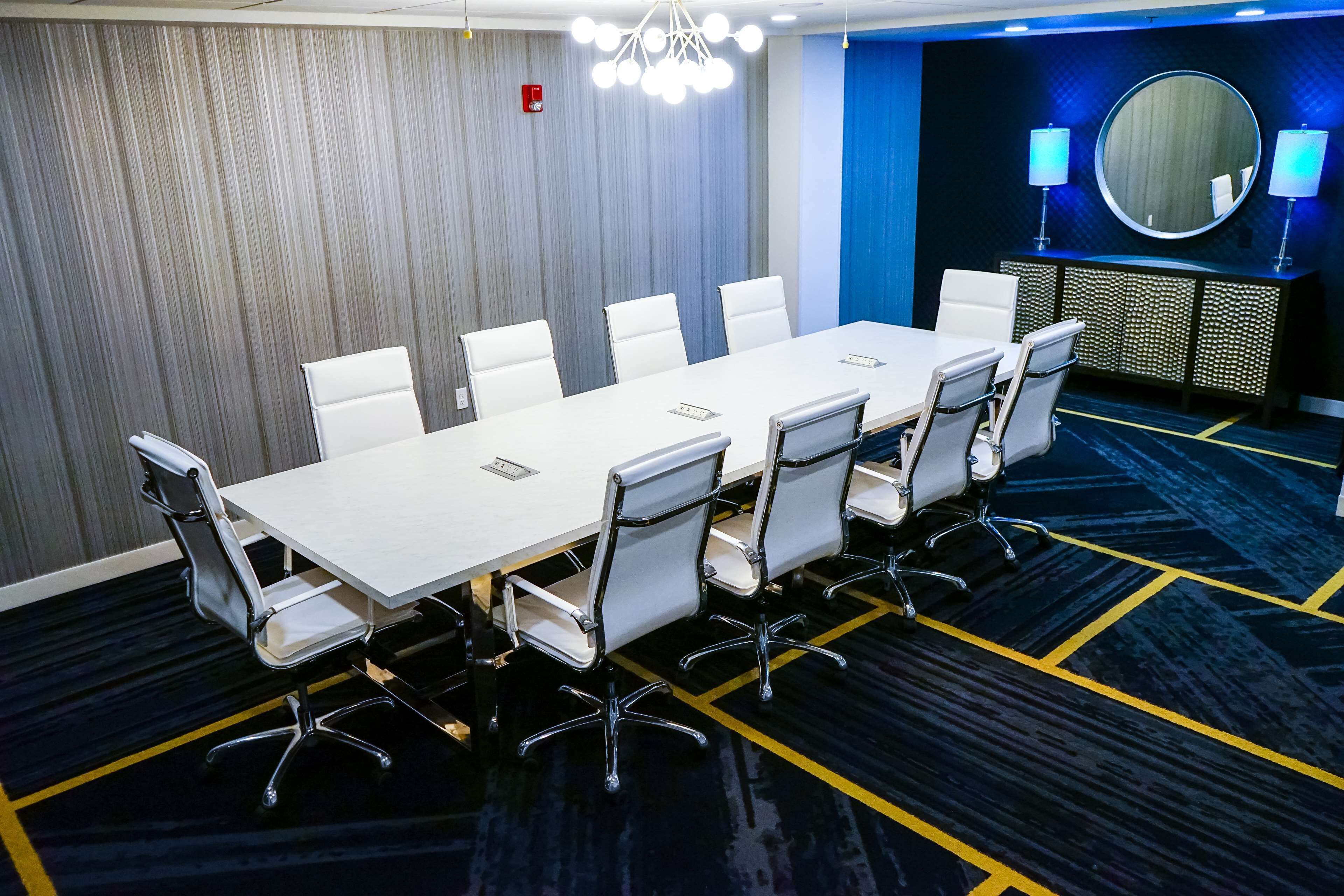 Una sala de conferencias con una larga mesa, sillas blancas, un espejo redondo y una pared azul decorativa.