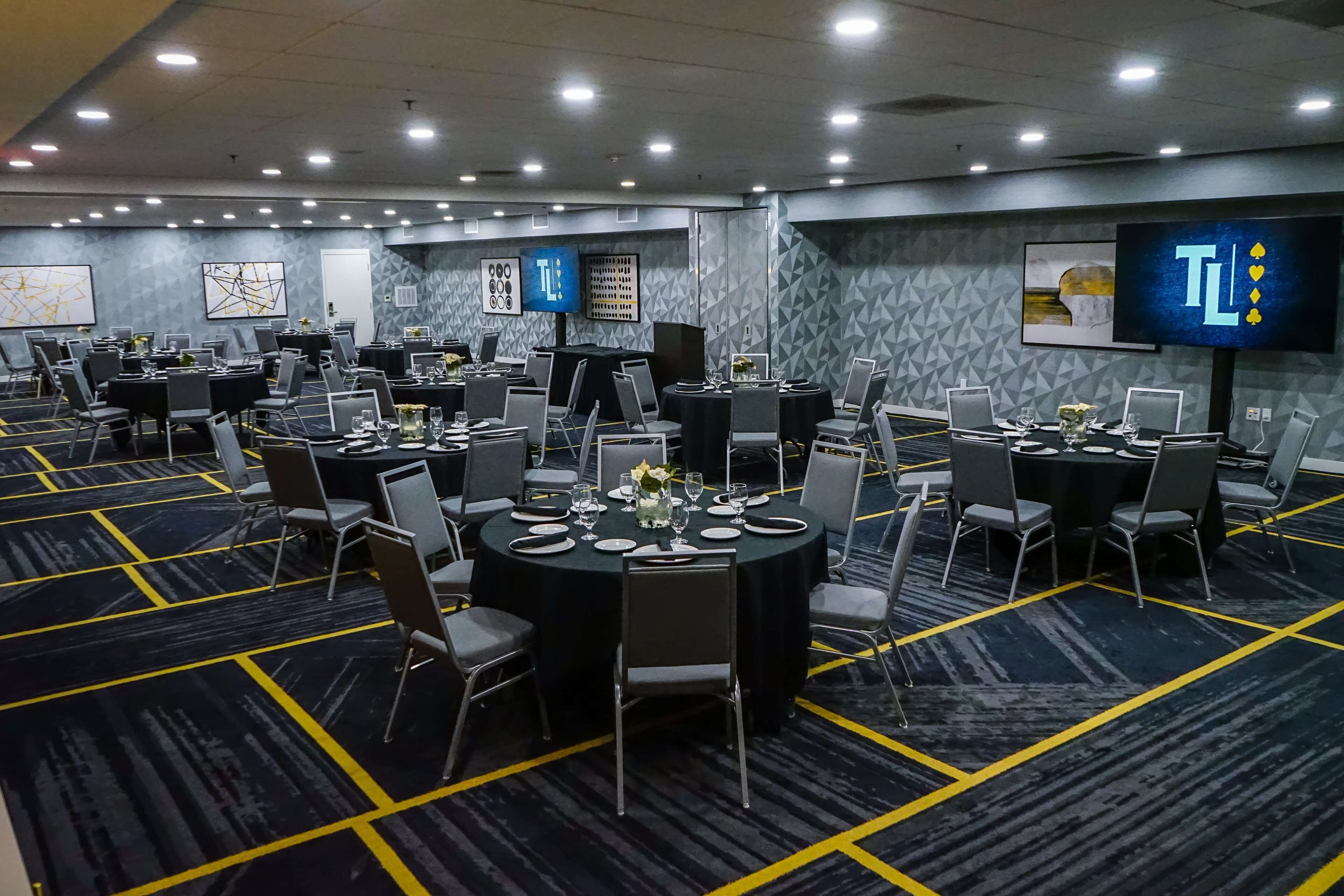 A conference room with multiple tables, chairs, and a large screen.