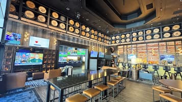 A bar area with multiple seating options, a television screen displaying sports, and a wall adorned with numerous bottles.